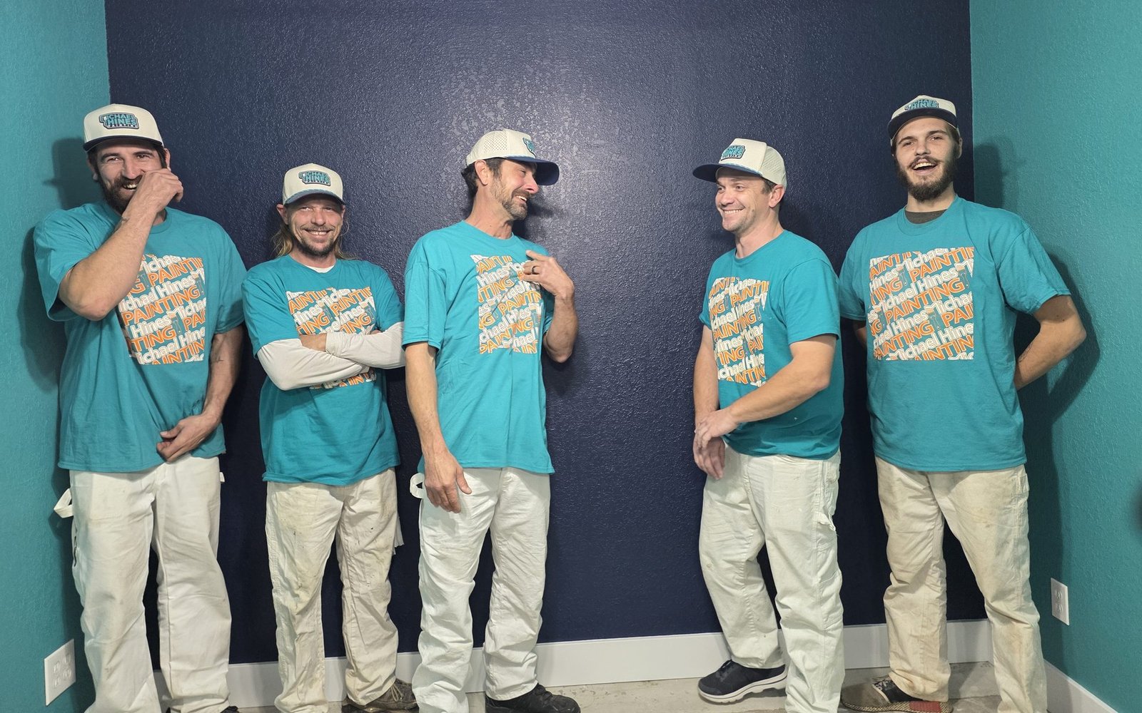 The Michael Hines Painting crew laughing together in company shirts and caps