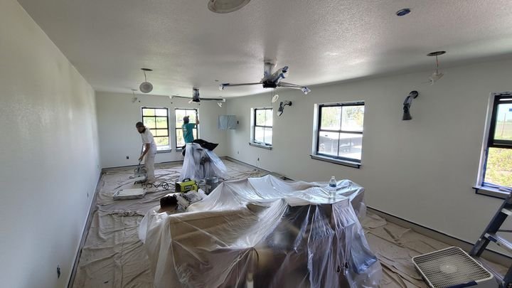 A painting crew at work in a living room with furniture covered and floors protected