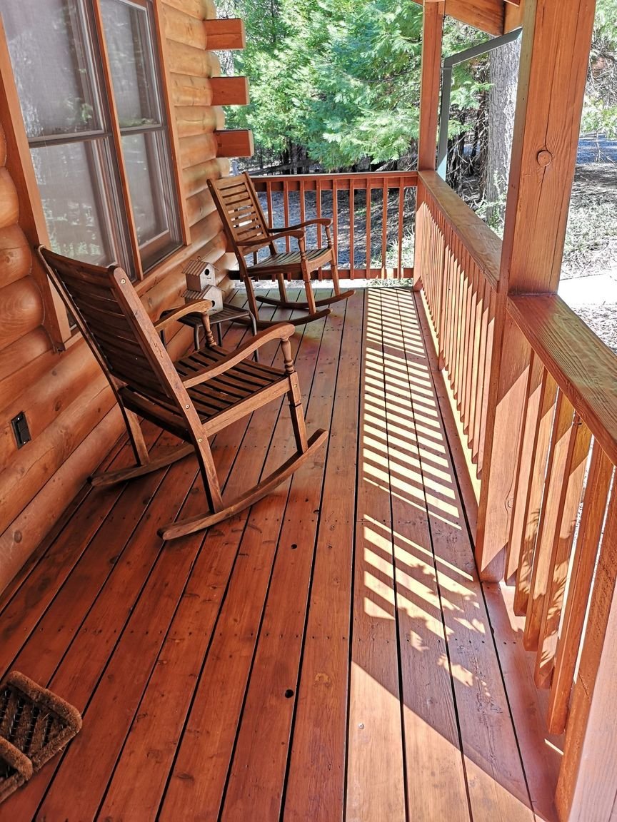 A finished cabin porch deck stained a rich mahogany, rocking chairs in the dappled light
