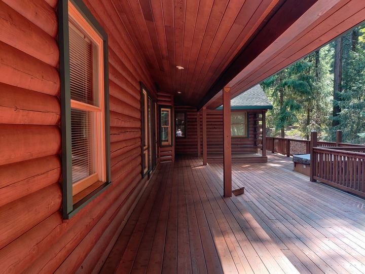 A finished wraparound cabin deck stained warm cedar, the covered space swept clean at the end of the job