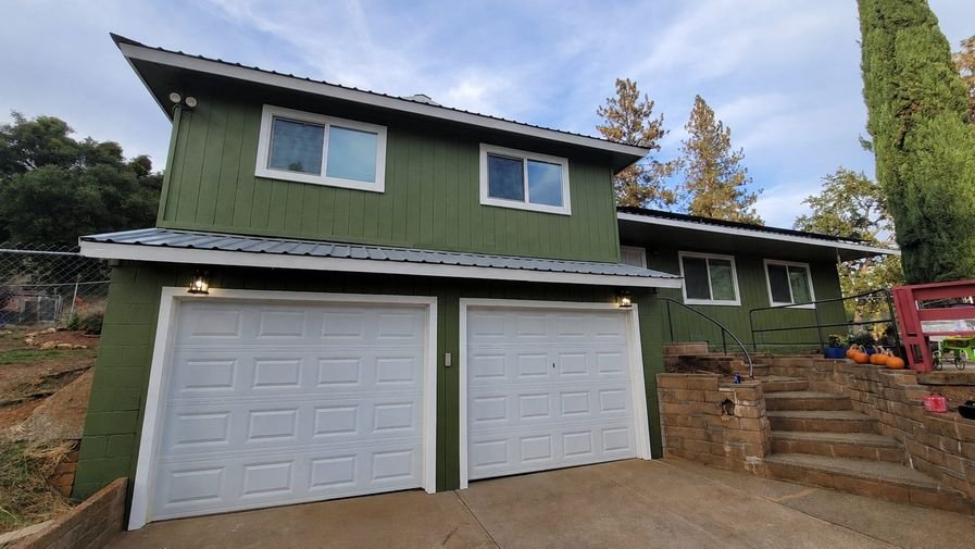 The same house freshly repainted a deep green with clean white trim around the windows and garage doors
