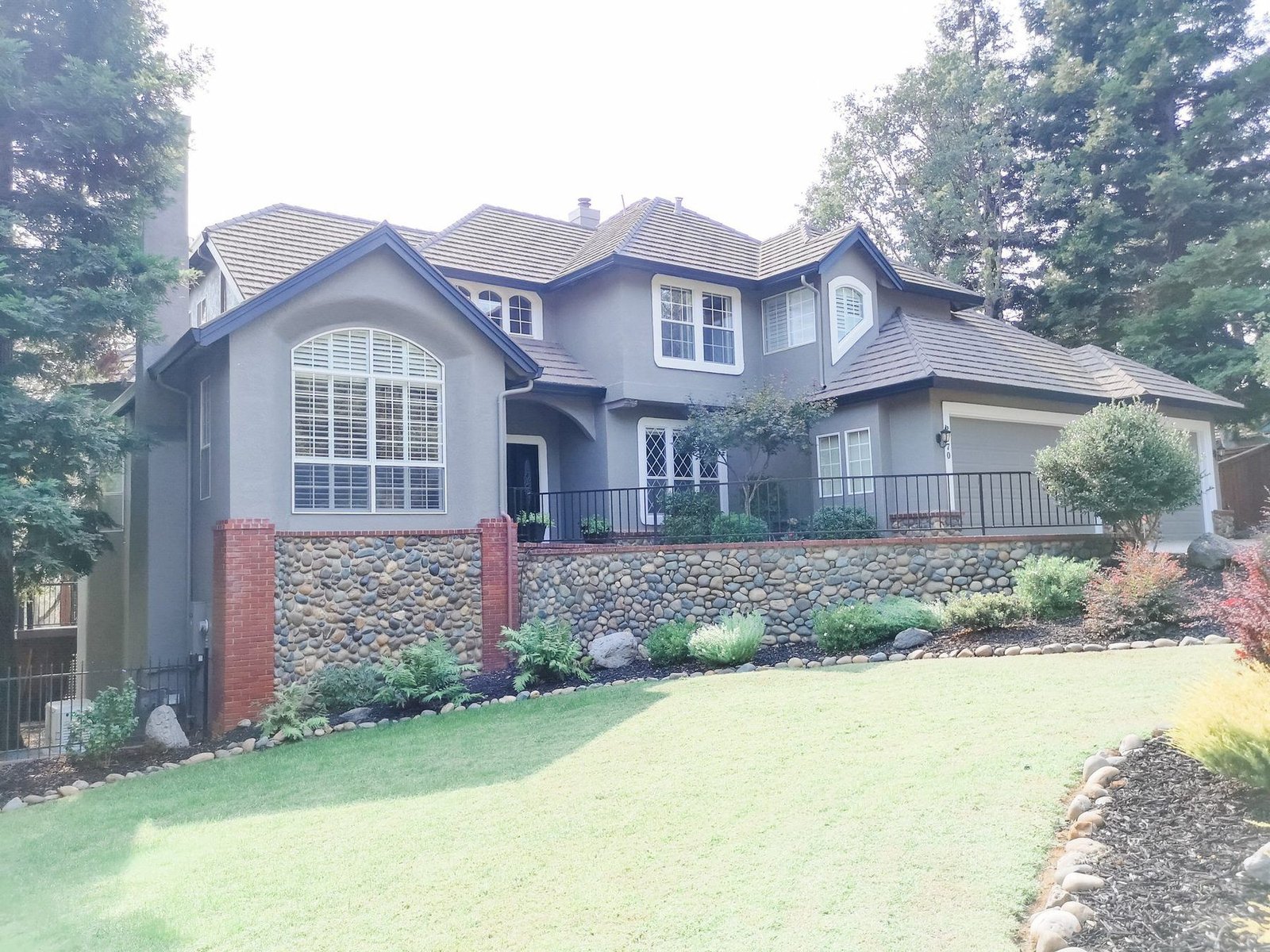 A stately two-story foothill home freshly repainted in gray with crisp white trim, framed by tall pines
