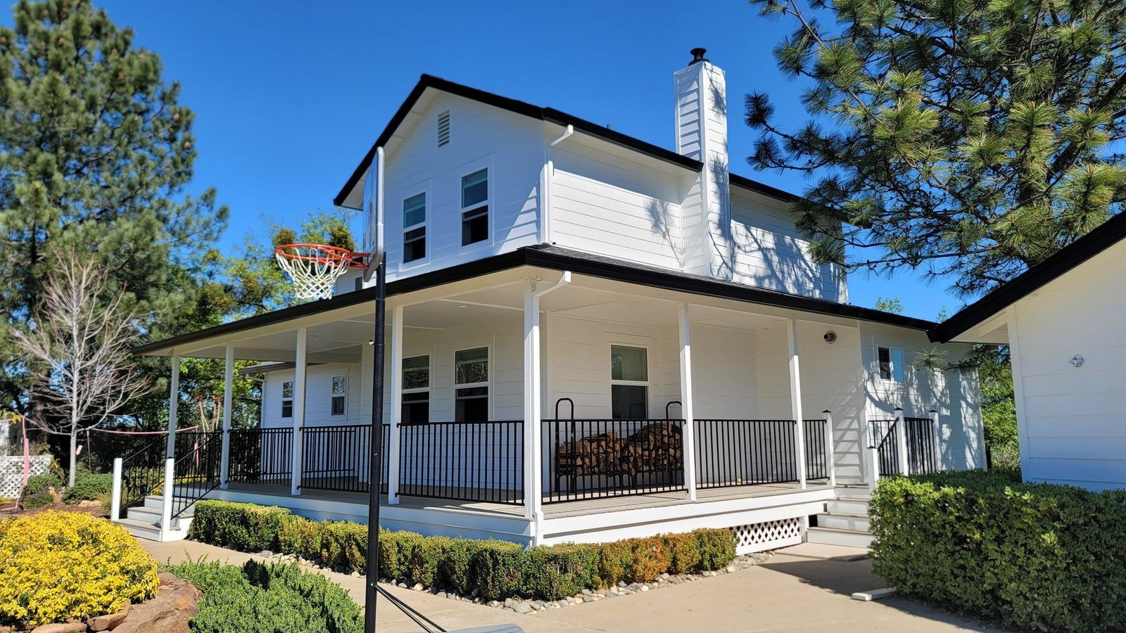 A two story white farmhouse with a wraparound porch, freshly repainted, under a clear sky