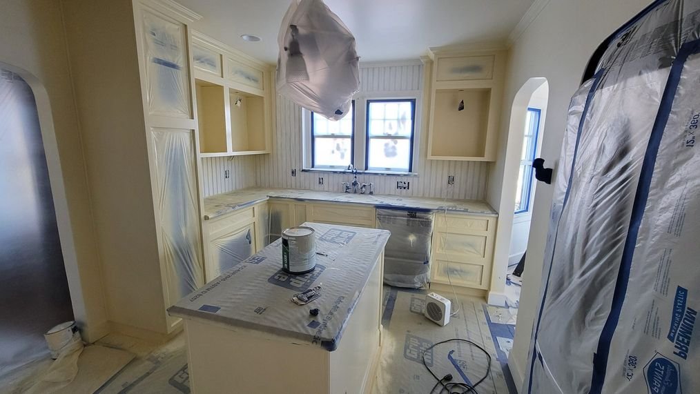 A kitchen fully masked for cabinet painting, with counters, floors and appliances covered in protective film and paper